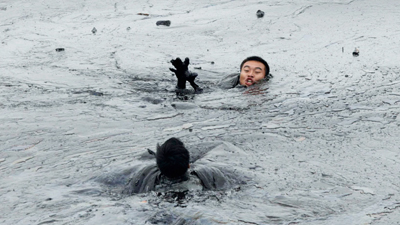 Workers attempt to rescue a firefighter from drowning in the oil slick during the oil spill clean-up operations at Dalian's Port on July 20, 2010. (REUTERS/Jiang  He/Greenpeace)